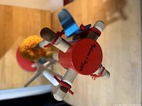 Top view of red circular wooden stand with four wooden handles inserted, showing Melissa and Doug logo on the stand.