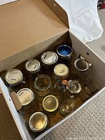 Overhead view of a cardboard box containing 14 assorted glass jars, different sizes and shapes, some with lids and some without.