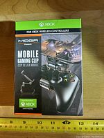 Front of boxed MOGA mobile gaming clip packaging showing product image, Xbox compatibility, and branding.