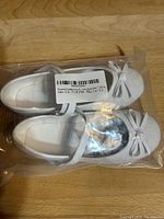 Pair of new toddler size 11 white Mary Jane shoes with shimmering finish, shown inside plastic packaging.
