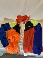 Photo of Nike multicolor block track jacket showing front with orange, red, blue, yellow, and black panels and white zipper.