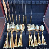 Open wooden box displaying gold-toned knives, forks, and spoons organized within black fabric lining.