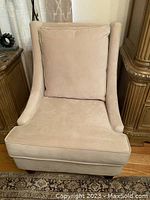 Front view showing beige faux suede upholstery, loose back cushion, and curved armrests.