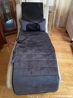 Full view of gray Comfier massage mat laid out on a beige chaise lounge with controller and pillow visible