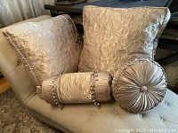Photo showing two square embossed floral damask cushions, one cylindrical bolster pillow with beaded trim, and one round pleated satin cushion.