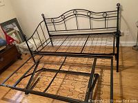 Front view of black metal daybed frame with trundle separated on hardwood floor