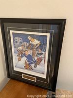 Framed print on a wooden table showing artwork of NHL goalies in vintage gear on ice.