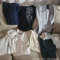 Photo of assorted women's clothing displayed on a sofa including sweaters, pants, and tops in various colors such as gray, black, and white.
