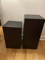 Photo showing two black cube-shaped plant stands of different heights on a wooden floor against a wall.