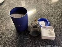 Blue original Swarovski packaging with black foam holder for the snowflake ornament, the ornament itself, and the white jewelry box containing the necklace.