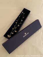 Rose gold tone necklace with butterfly pendant displayed inside navy blue Swarovski box, with lid placed next to box.