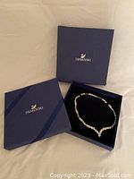 Closed blue Swarovski box alongside blue box with necklace on black velvet insert.