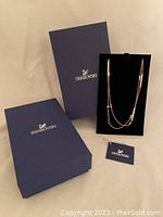 Swarovski necklace displayed with original packaging including two blue Swarovski boxes and a tag.