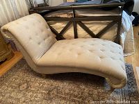 Side view of tufted armless chaise lounge showing curved profile, button tufting, off-white upholstery and wood feet