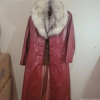 Full view of the burnt red leather coat with fox fur collar hanging against a plain background.