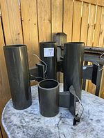 Four black cylindrical wall-mounted outdoor lights on a table against a wooden fence showing overall size and shape.