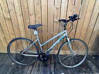 Side view of the silver CCM bicycle showing the full 17 inch frame, pedals, seat, and tires on wooden deck with wooden fence background.