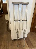 Front view of two aluminum crutches with padded armrests and hand grips, standing upright against a door.