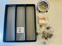 Cutlery holder tray with three compartments, small round clock, string of light bulbs, and pop up cups on white surface.