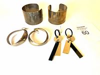 Photo showing two wide gold-tone cuff bangles and two pairs of earrings, one twisted oval hoop style and one geometric drop style, all arranged on a white background with lot number