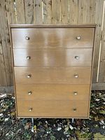 Front view of the Imperial MCM wood tallboy chest highlighting the five drawers with metal knob handles.