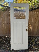 Front view of old wooden door painted white with glass panel and three recessed rectangular panels below.