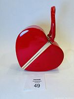 Front and side view of the red glossy heart-shaped purse showing gold-tone frame and red wrist strap.