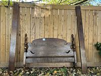 Full view of the disassembled vintage double bed frame parts against a wood fence including headboard, footboard, and long side rails.