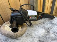 Black Wen 7-inch sander polisher with an attached wool polishing pad lying on a surface, power cord coiled loosely.