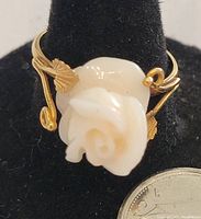 Close-up front view of the 18K gold ring showcasing the white carved coral rose and gold leaf details, with a coin for scale.
