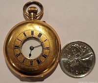 Front cover closed showing applied Roman numeral chapter ring and winding crown next to a coin for scale