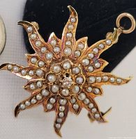 Front view of starburst pendant/brooch showing yellow gold rays set with seed pearls and central diamond