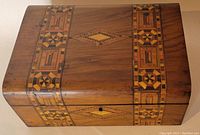 Top view of the rectangular wooden writing box displaying geometric inlay patterns characteristic of Tunbridge ware, with two vertical bands and central diamond motif in various wood tones.