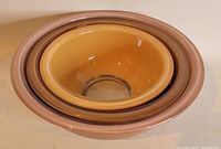 Three nested Pyrex mixing bowls in autumn colors: mustard yellow, light brown, and mauve.