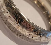 Close-up photo showing detailed engraved floral and scroll pattern on sterling silver bangle.