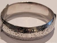 Front view showing detailed floral and leaf engraving on the sterling silver bangle with attached safety chains.