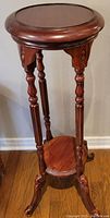 Side angled view of the full wooden plant stand showing round top surface, carved legs, and lower shelf.