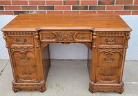 Front view of the walnut desk with two pedestal bases showing carved drawer fronts and brass handles, highlighting overall design and proportion.