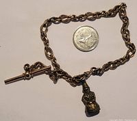 Full view of a gold filled watch chain with toggle clasp, featuring an engraved charm next to a quarter for size reference.