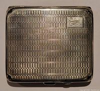 Top exterior view of the cigarette case showing detailed engraved wave and basket weave pattern and monogram initials in a rectangular cartouche on upper right corner.