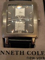 Close-up front view of Kenneth Cole watch face with square stainless steel case and black textured dial.