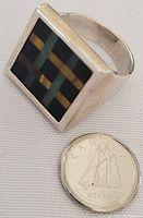 Front and top view of men's sterling silver ring with rectangular multi-colored stone inlay placed beside a quarter for size reference.