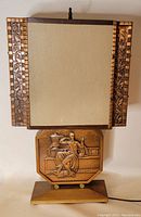 Front view of MCM lamp showing copper repoussé work on square shade and detailed figure on base panel.