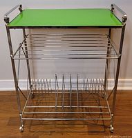 Full front view of the green LP record stand showing chrome frame and wire racks for storage.
