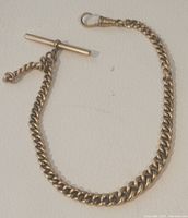Rolled gold vintage watch chain laid flat on surface showing curb link design and T-bar clasp