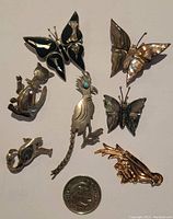 Top view of seven animal pins showing front details and materials such as inlay and turquoise accents. Coin included for size reference.