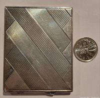 Top view of the compact mirror showing the woven diagonal line pattern next to a coin for size reference.
