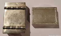 Two match safes side by side, showing size and surface details including scratches and decoration.