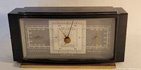 Front view of the rectangular black metal vintage barometer with temperature, barometer, and humidity dials visible under glass.