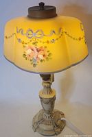 Front view of the lamp showing yellow glass shade with hand painted blue bows and pastel floral decorations, and the ornate painted cast metal base.